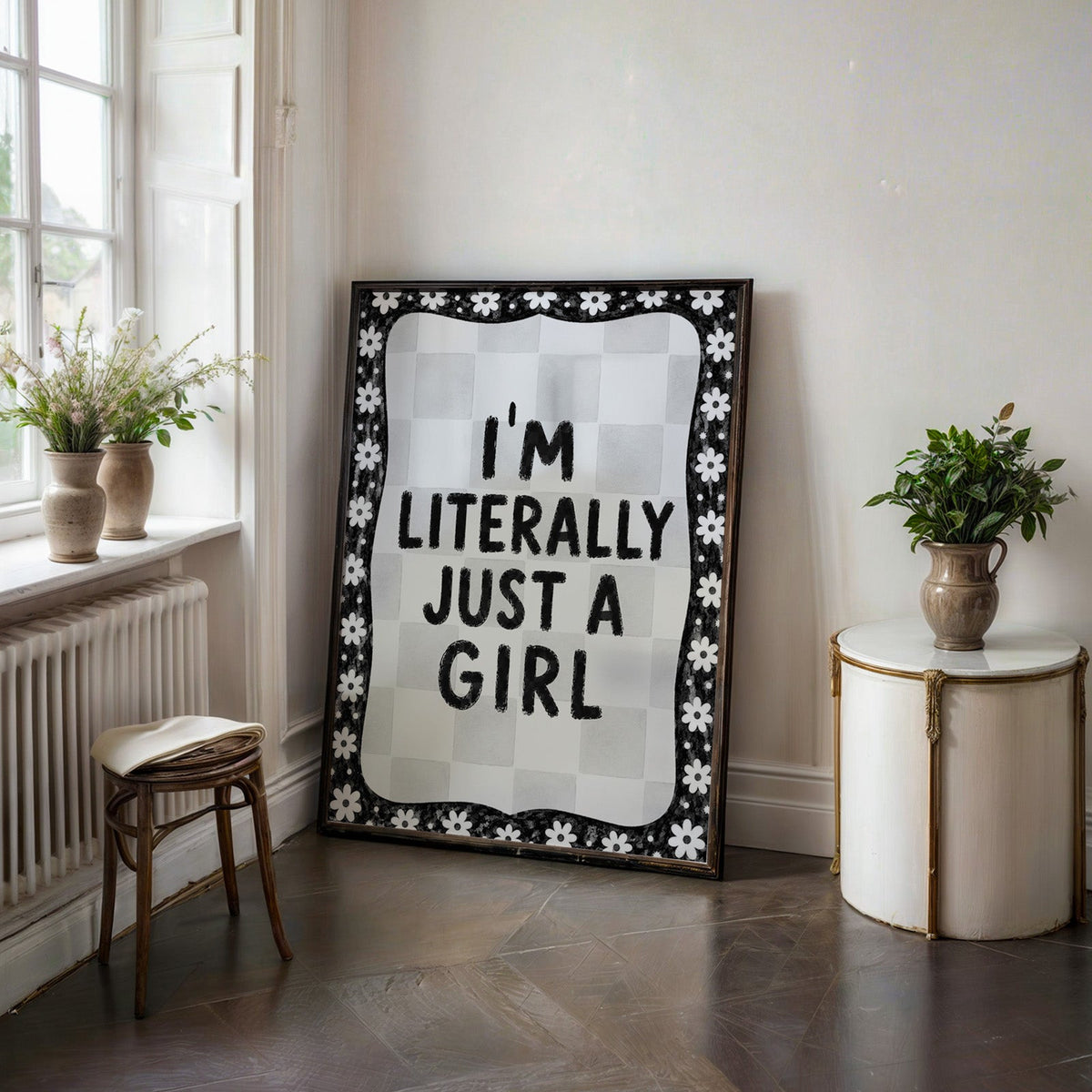 I'm literally just a girl quote with daisy border print in a black frame on a dark stone floor beside a white side table