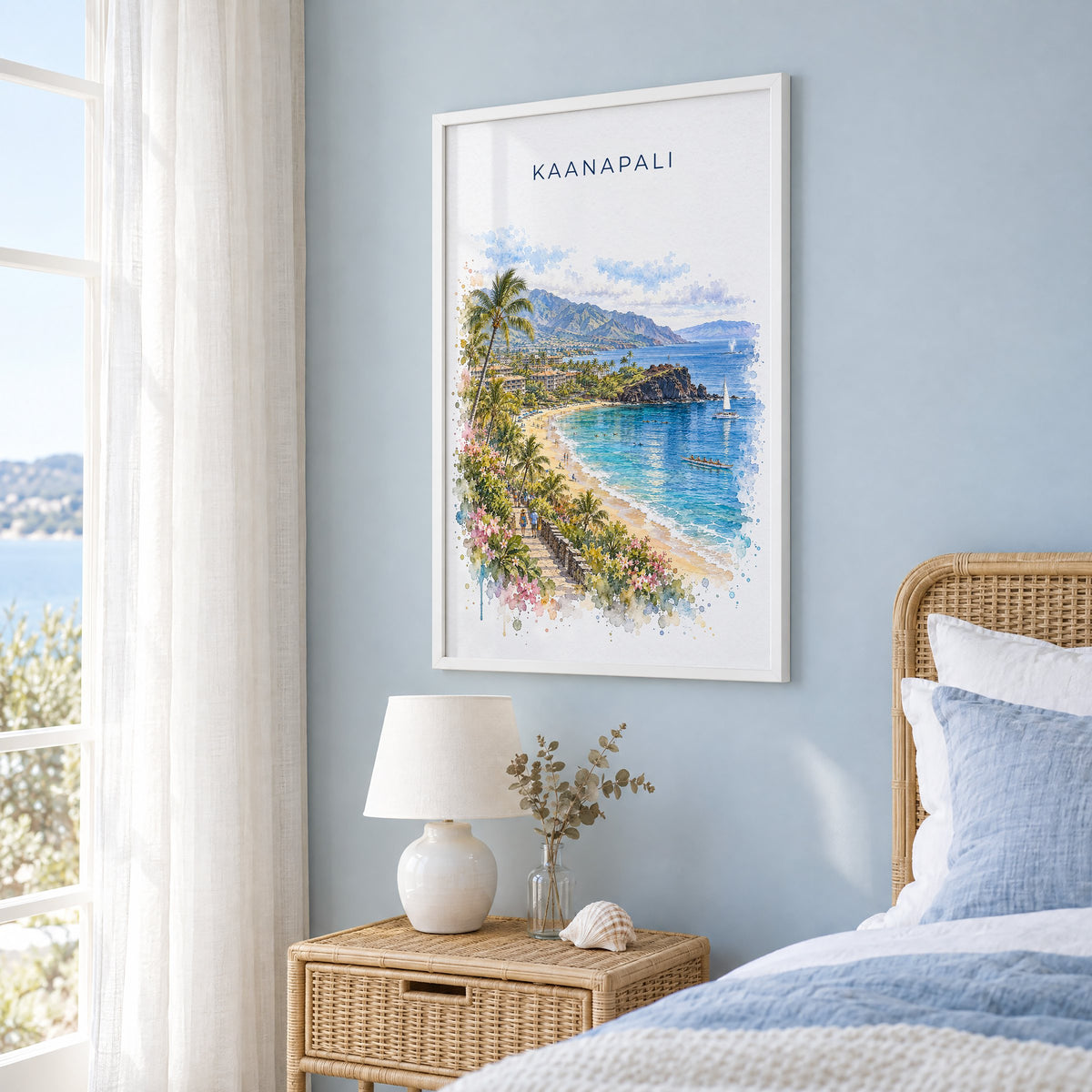 Kaanapali watercolor print in a white frame on a pale blue wall beside a rattan bed in a coastal bedroom
