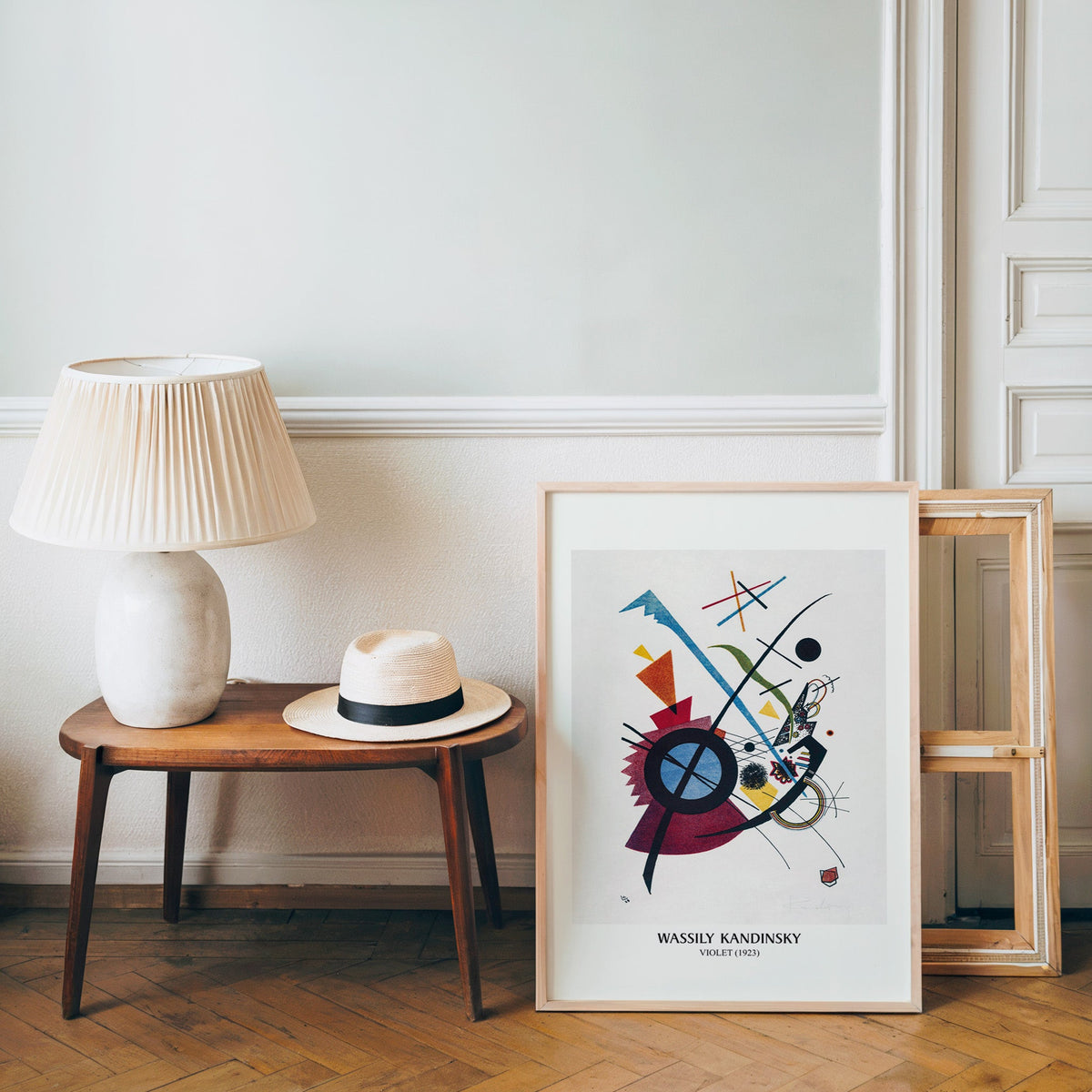 Bauhaus abstract poster in a light wood frame leaning by a bench and hat