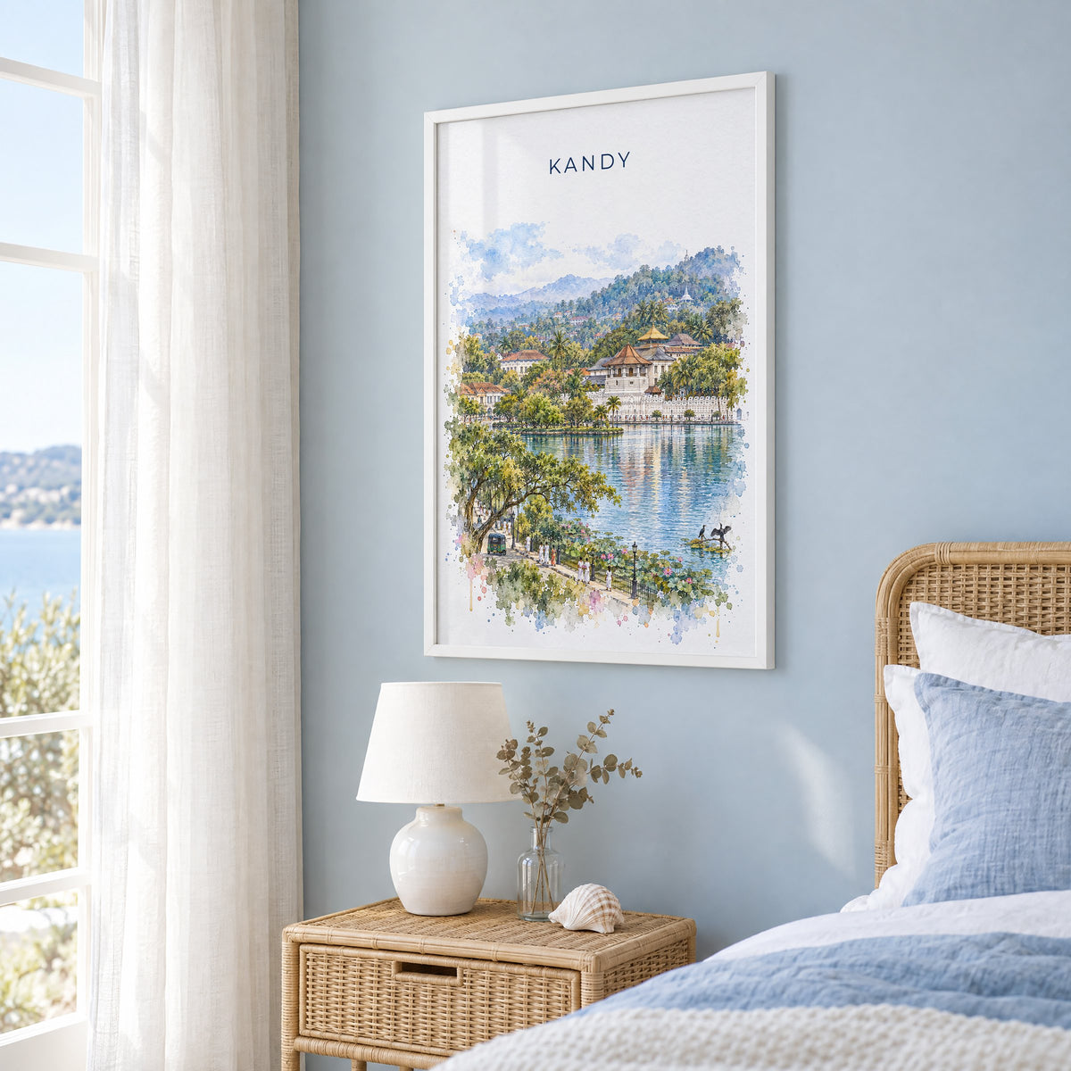 Kandy, Sri Lanka watercolor print in a white frame on a pale blue wall beside a rattan bed in a coastal bedroom