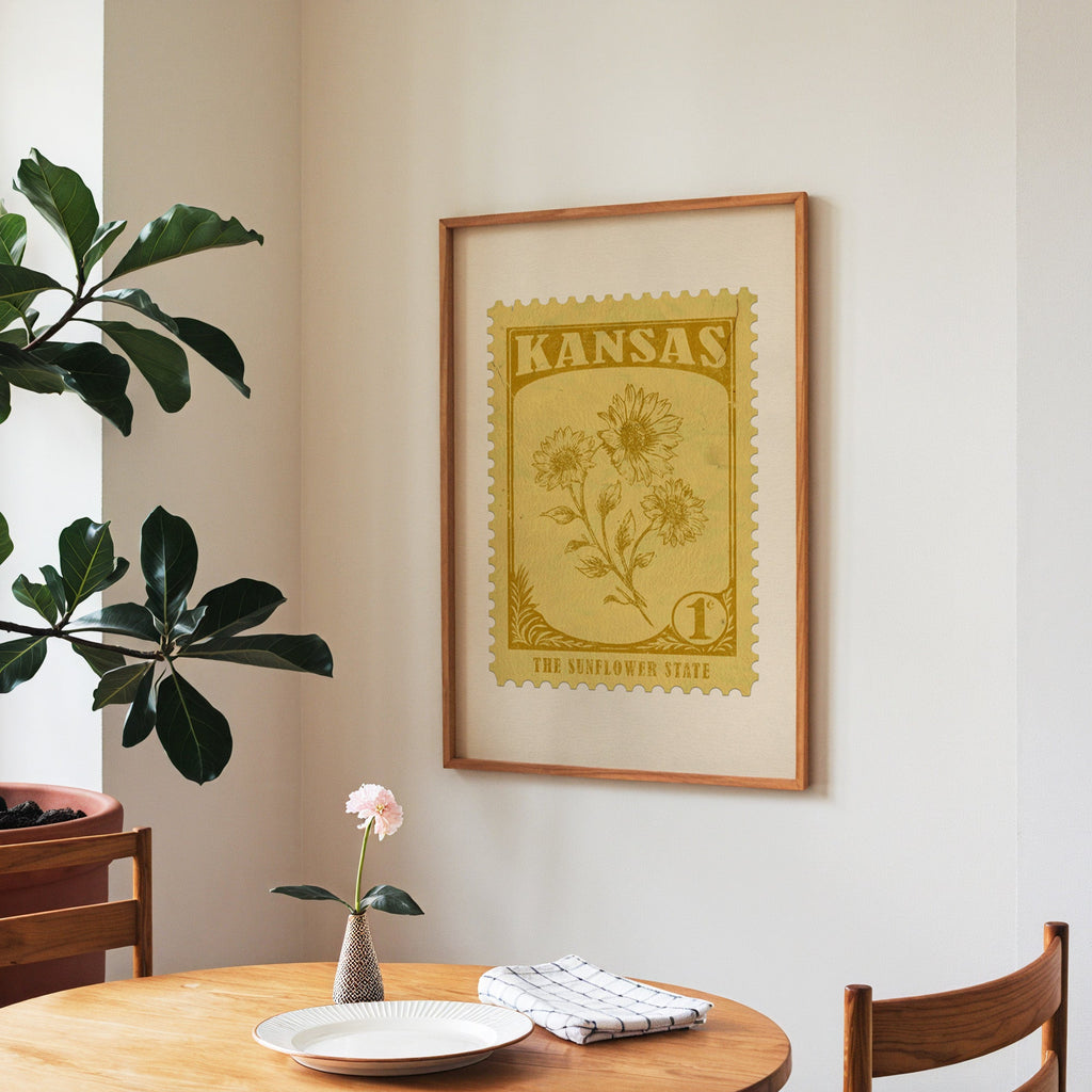 Kansas state flower print framed above a round wooden table with a single bloom in a vase and books