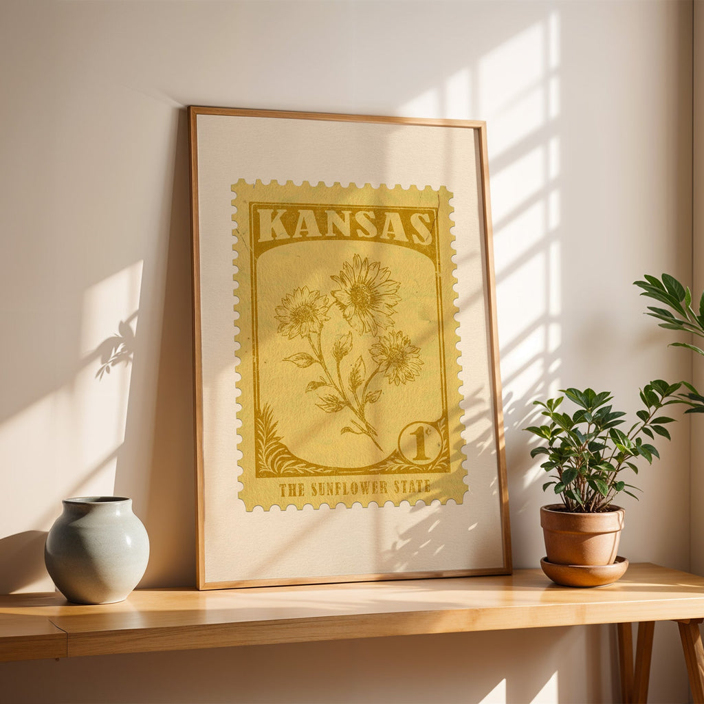 Kansas Sunflower stamp print in a light oak frame leaning on a wooden table beside a stoneware vase