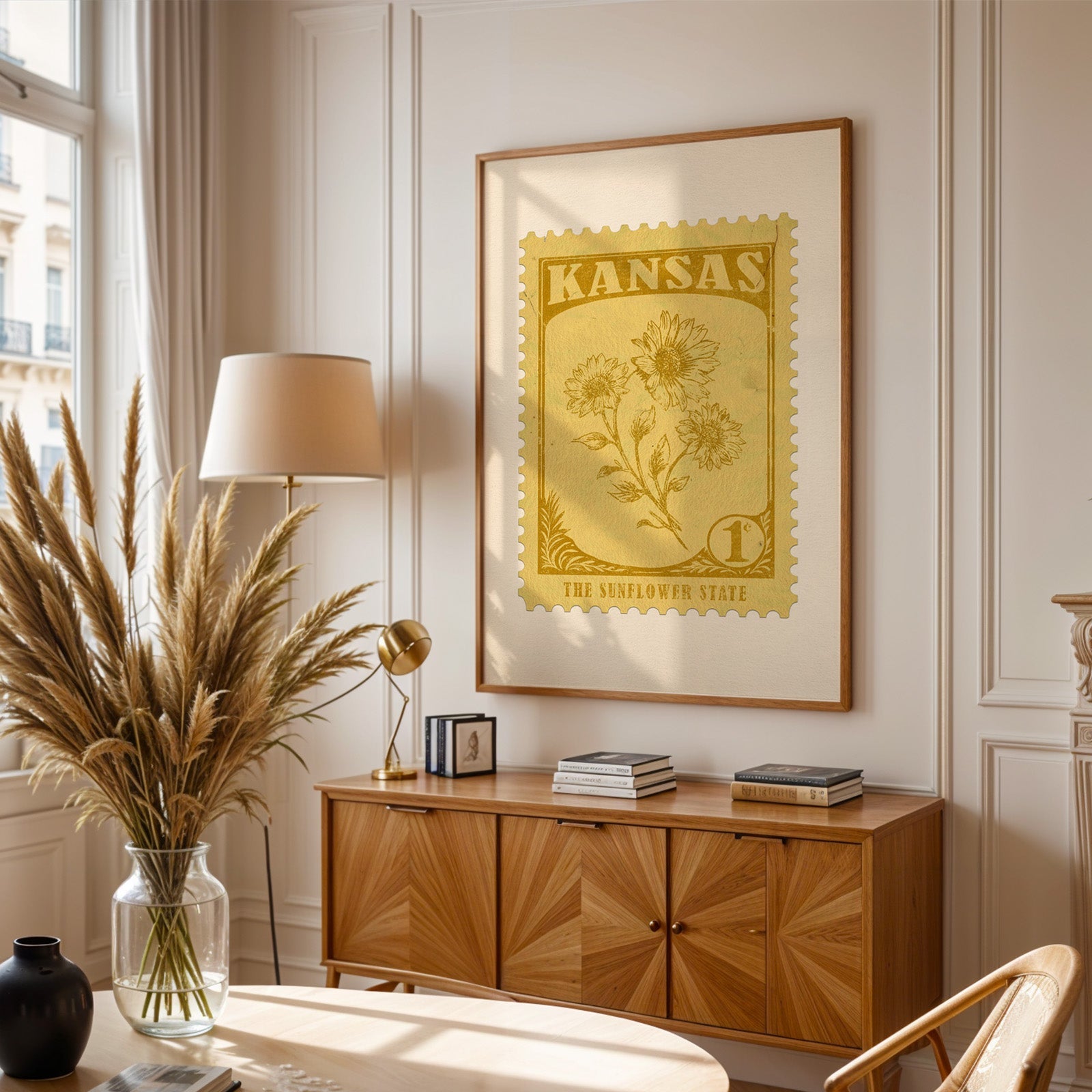 Kansas stamp print framed above a wooden sideboard, pampas grass in a glass vase and a floor lamp