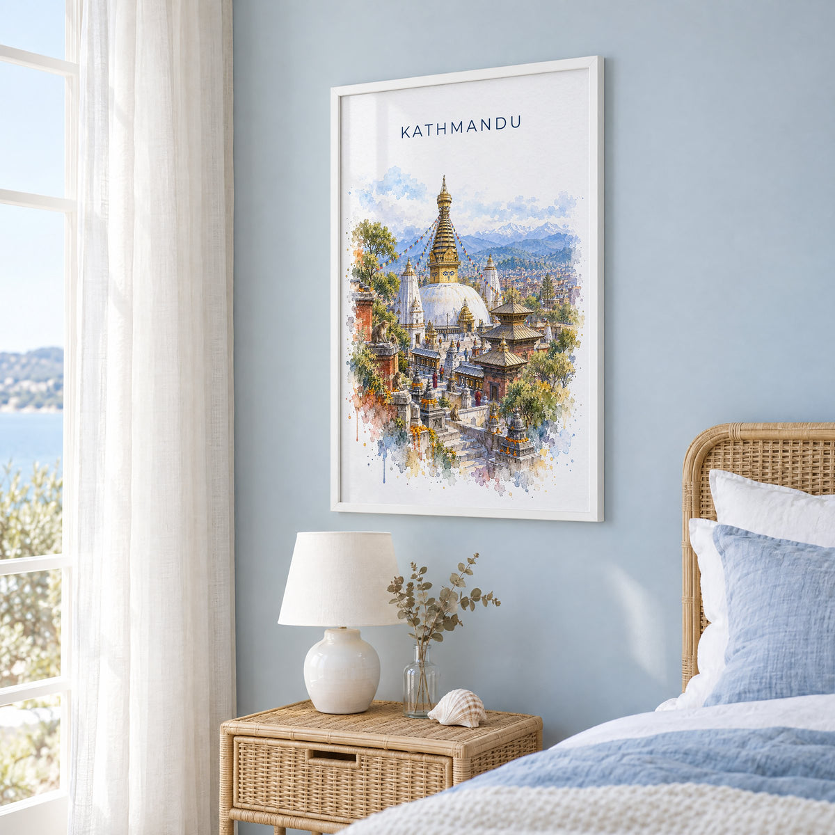 Kathmandu watercolor print in a white frame on a pale blue wall beside a rattan bed in a coastal bedroom