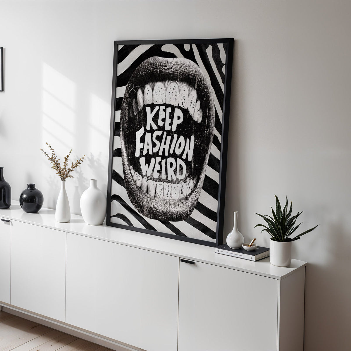 Halftone mouth with Keep Fashion Weird text print in a black frame on a white sideboard with black and white vases
