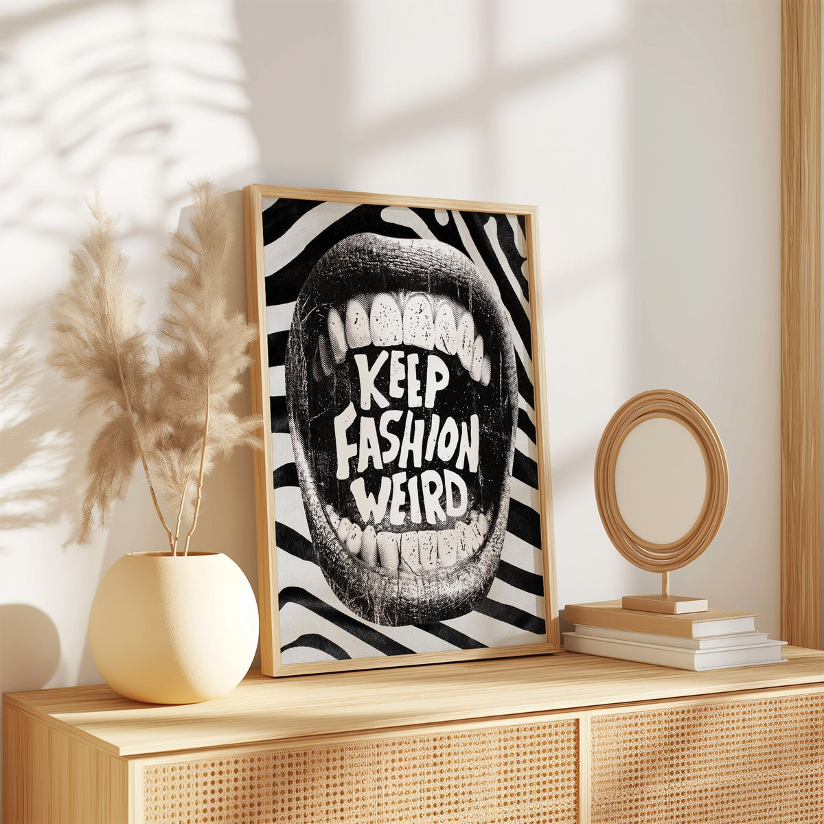 Halftone mouth with Keep Fashion Weird text print in an oak frame on a rattan sideboard beside pampas grass