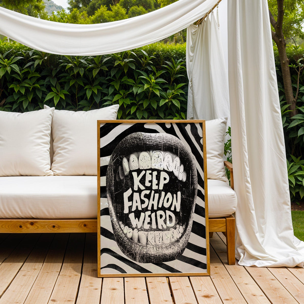 Halftone mouth with Keep Fashion Weird text print in an oak frame on an outdoor daybed under white drapes