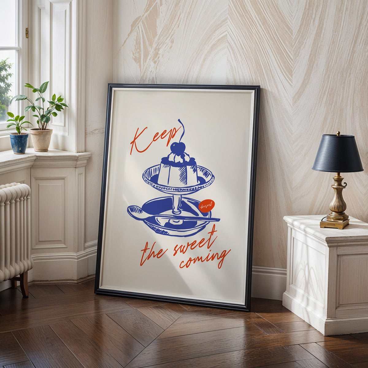 Keep the Sweet Coming flan print in a black frame on a dark herringbone floor