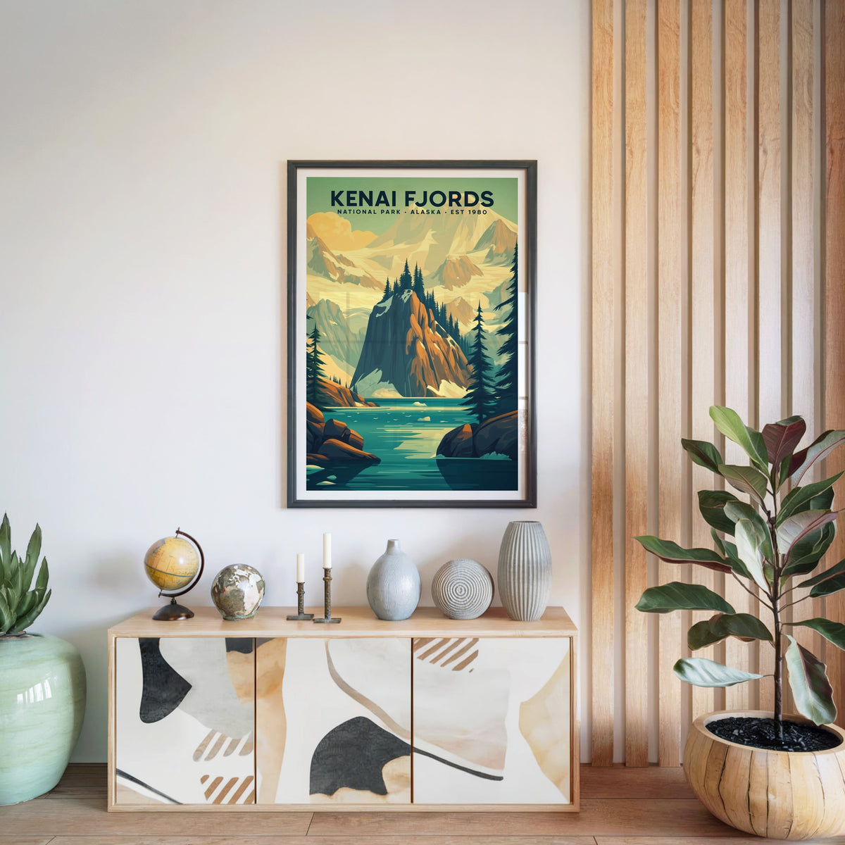 Kenai Fjords National Park print in a black frame above a light wood sideboard with a globe and ceramic vases