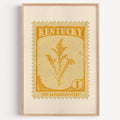 Kentucky state flower stamp print in marigold on cream, light oak frame on a plain white wall