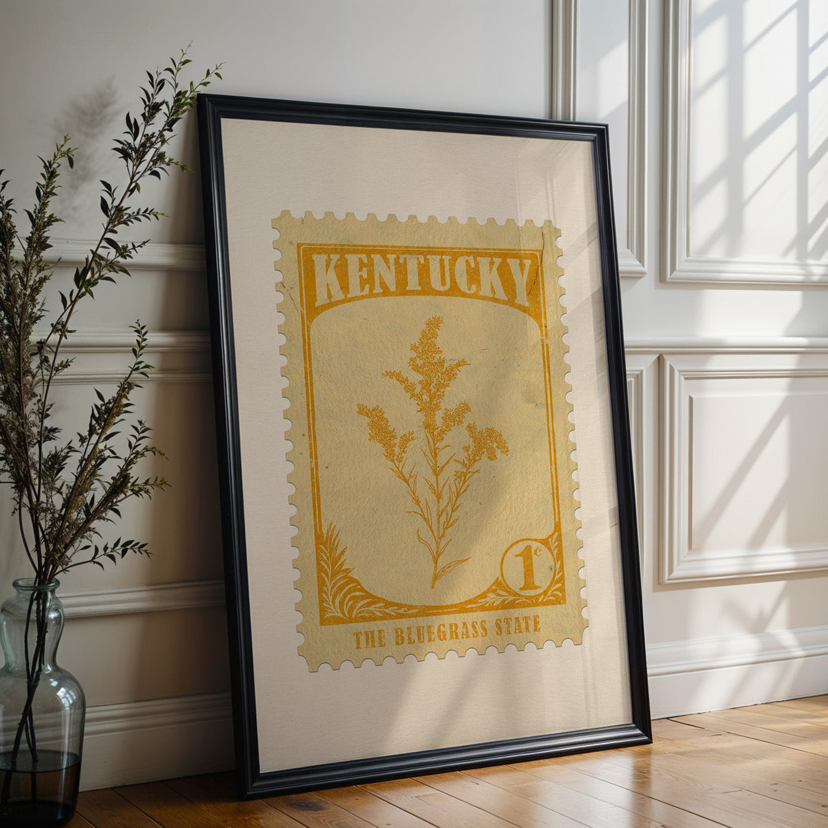Kentucky state flower print in a black frame leaning against a white panelled wall beside olive branches
