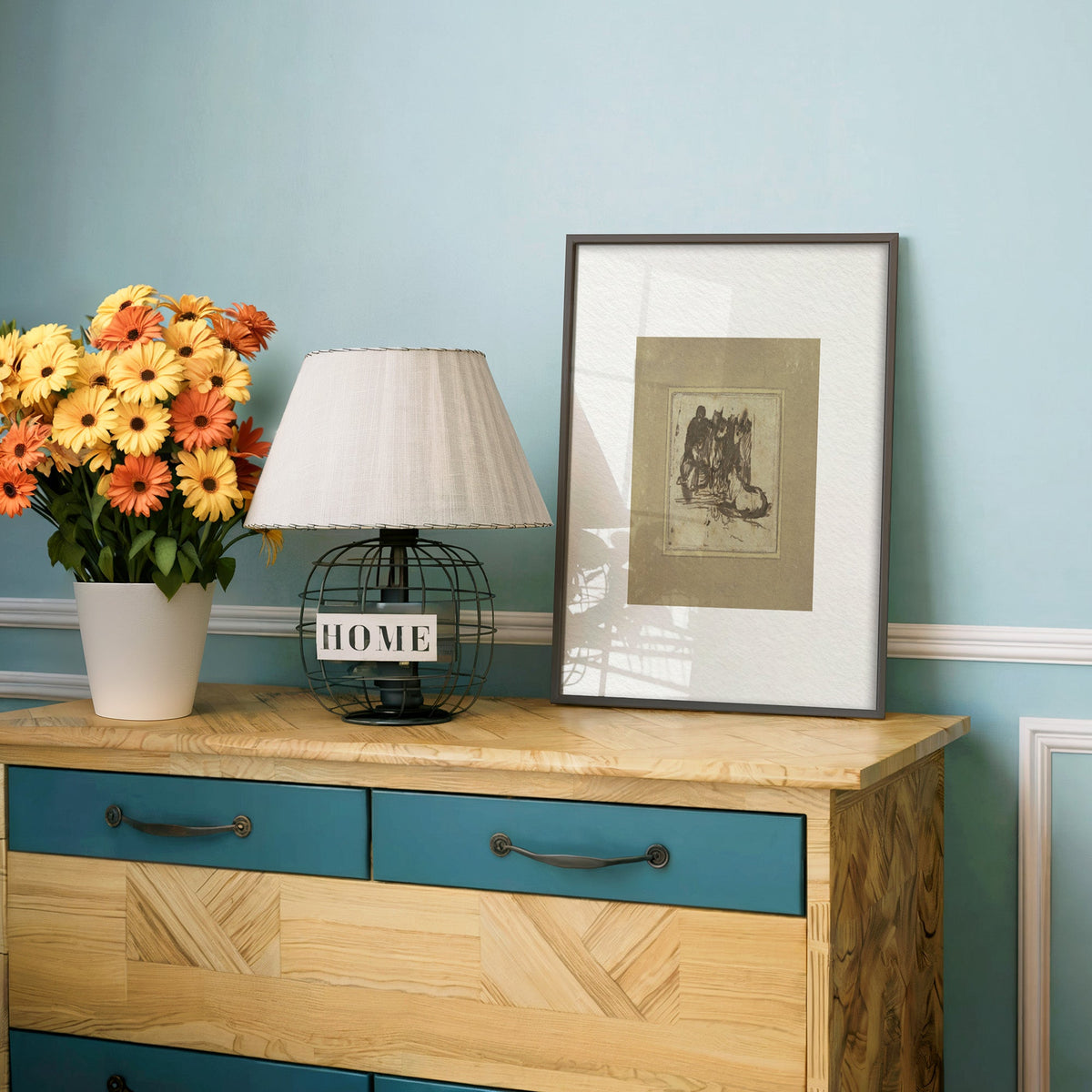Khaki mount ink sketch of figures print in a charcoal frame on a teal dresser beside orange and yellow daisies