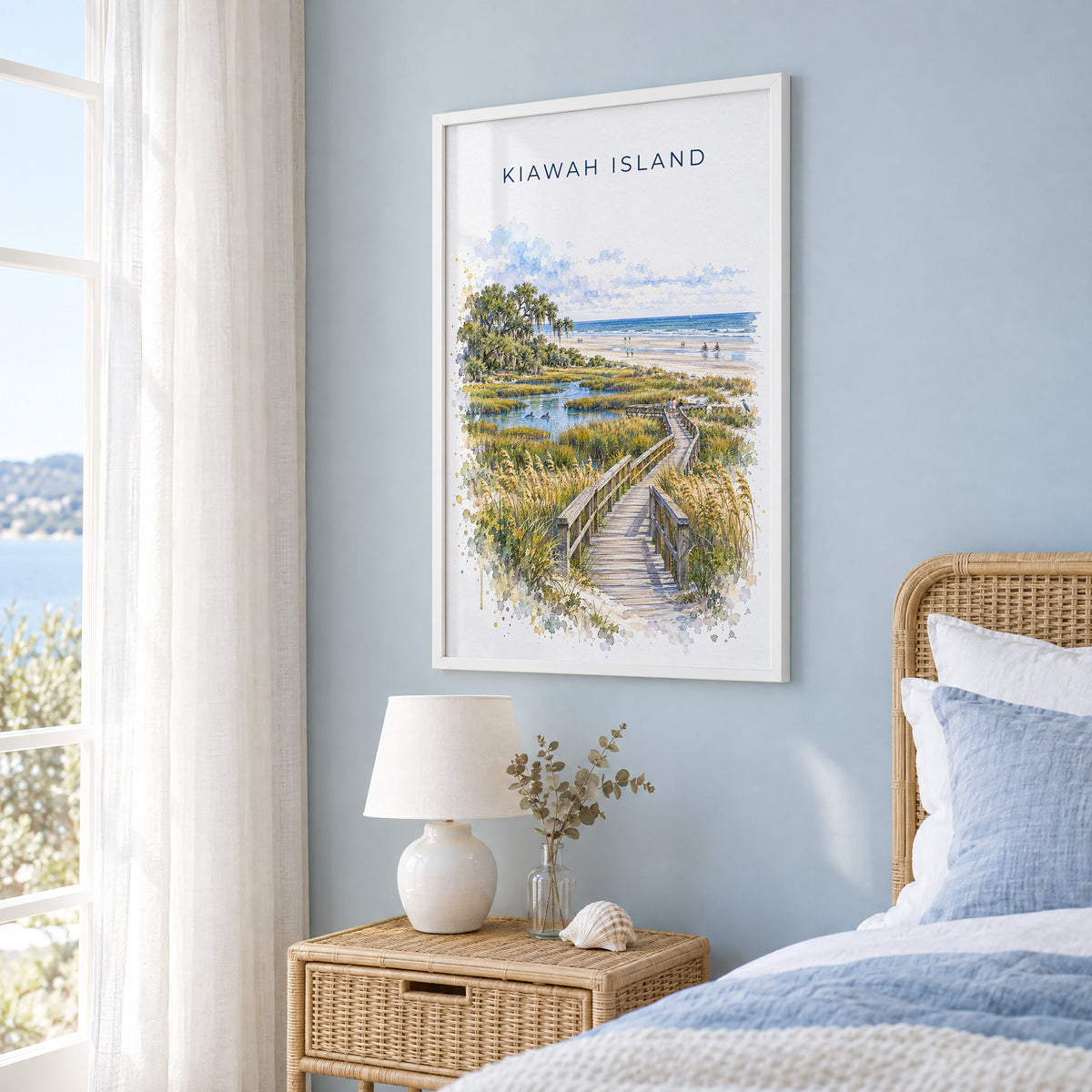 Kiawah Island watercolor print in a white frame on a pale blue wall beside a rattan bed in a coastal bedroom