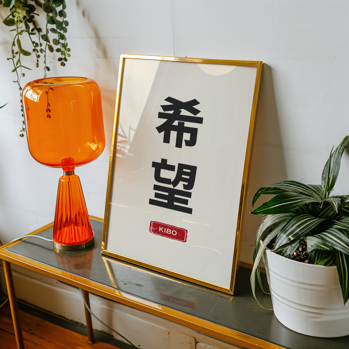 Kibo hope kanji red label print shown in a gold frame on a console beside an orange glass lamp