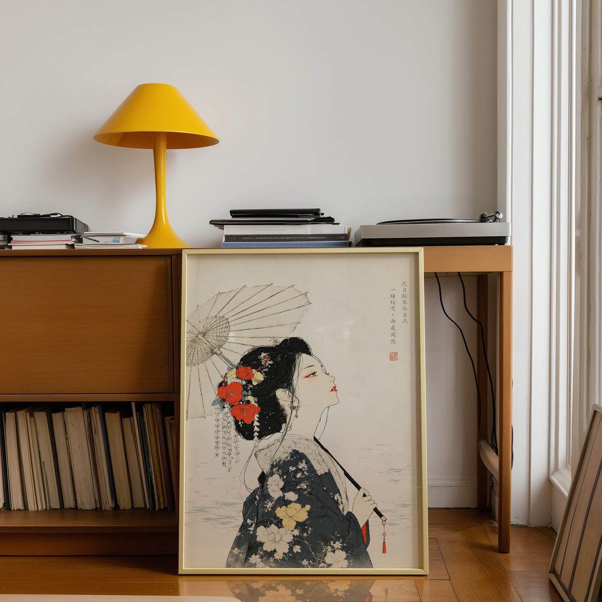 kimono woman with parasol and red flowers print shown in a gold frame leaning under a teak desk with a yellow lamp