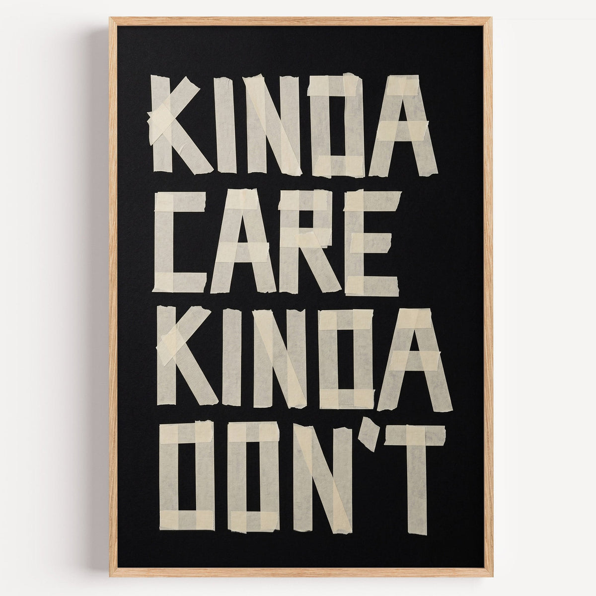 Kinda Care Kinda Don't paper tape letters on black print in a light oak frame on a plain white wall