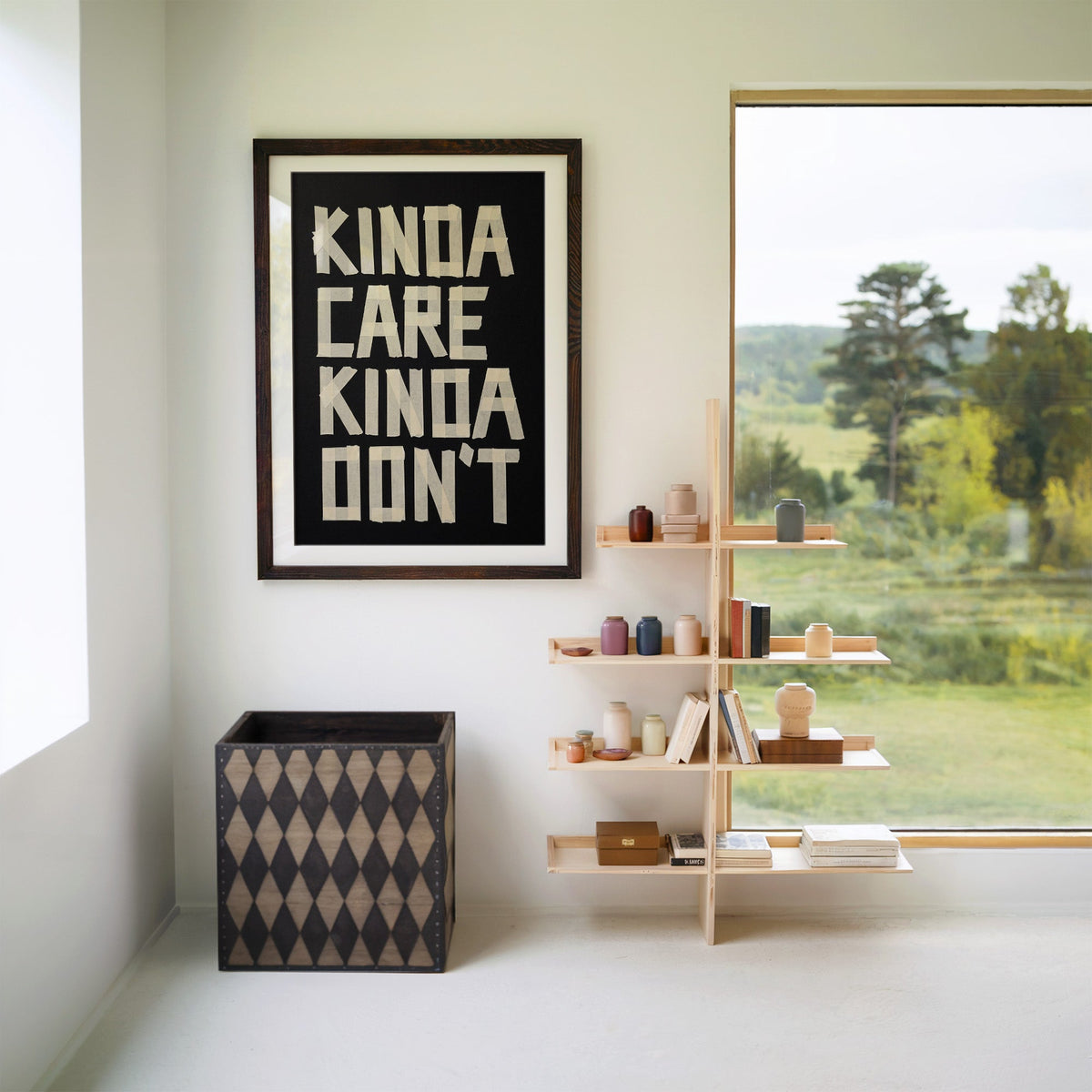 Kinda Care Kinda Don't paper tape letters on black print in a walnut frame with a white mat beside wooden shelves and a garden window