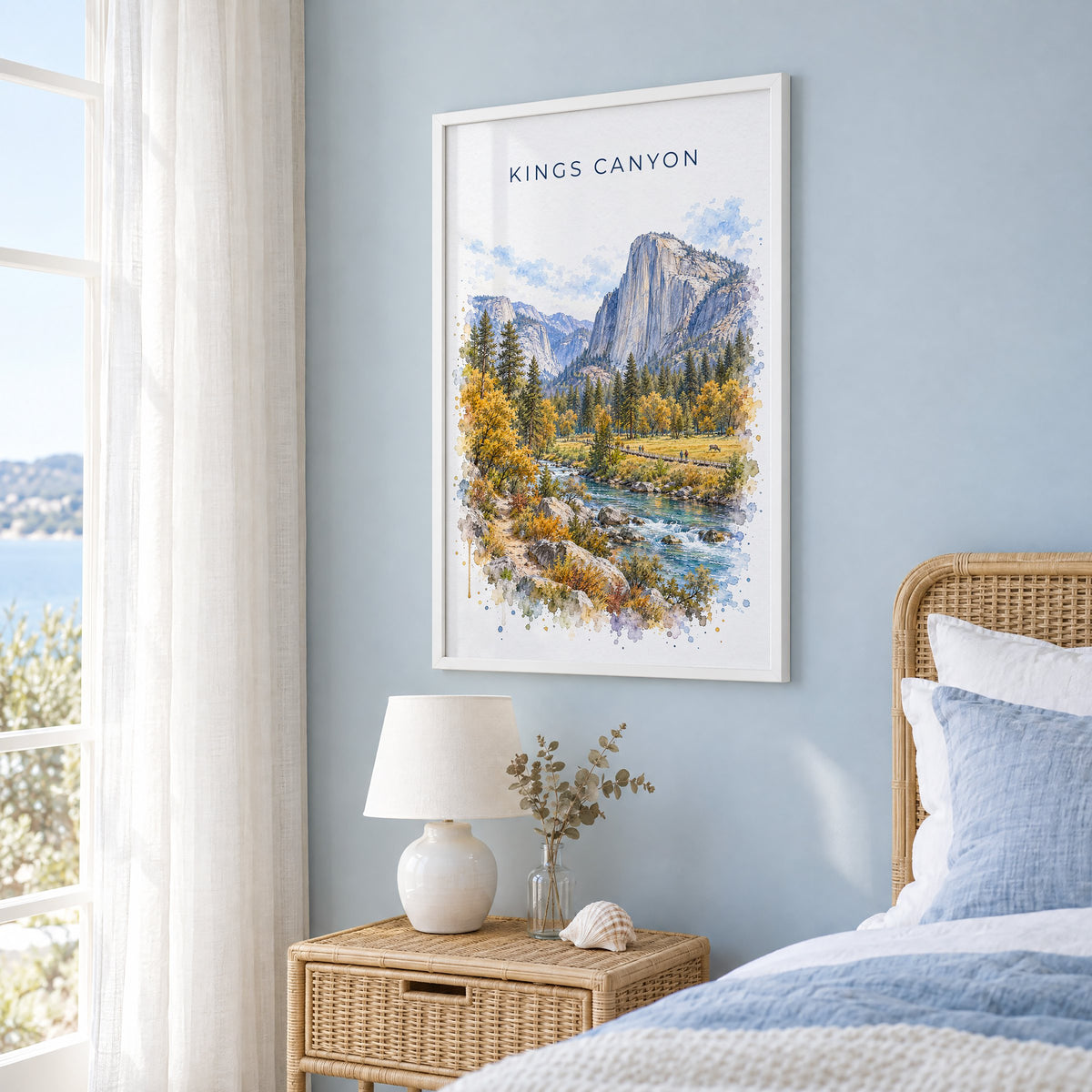 Kings Canyon National Park watercolor print in a white frame on a pale blue wall beside a rattan bed in a coastal bedroom