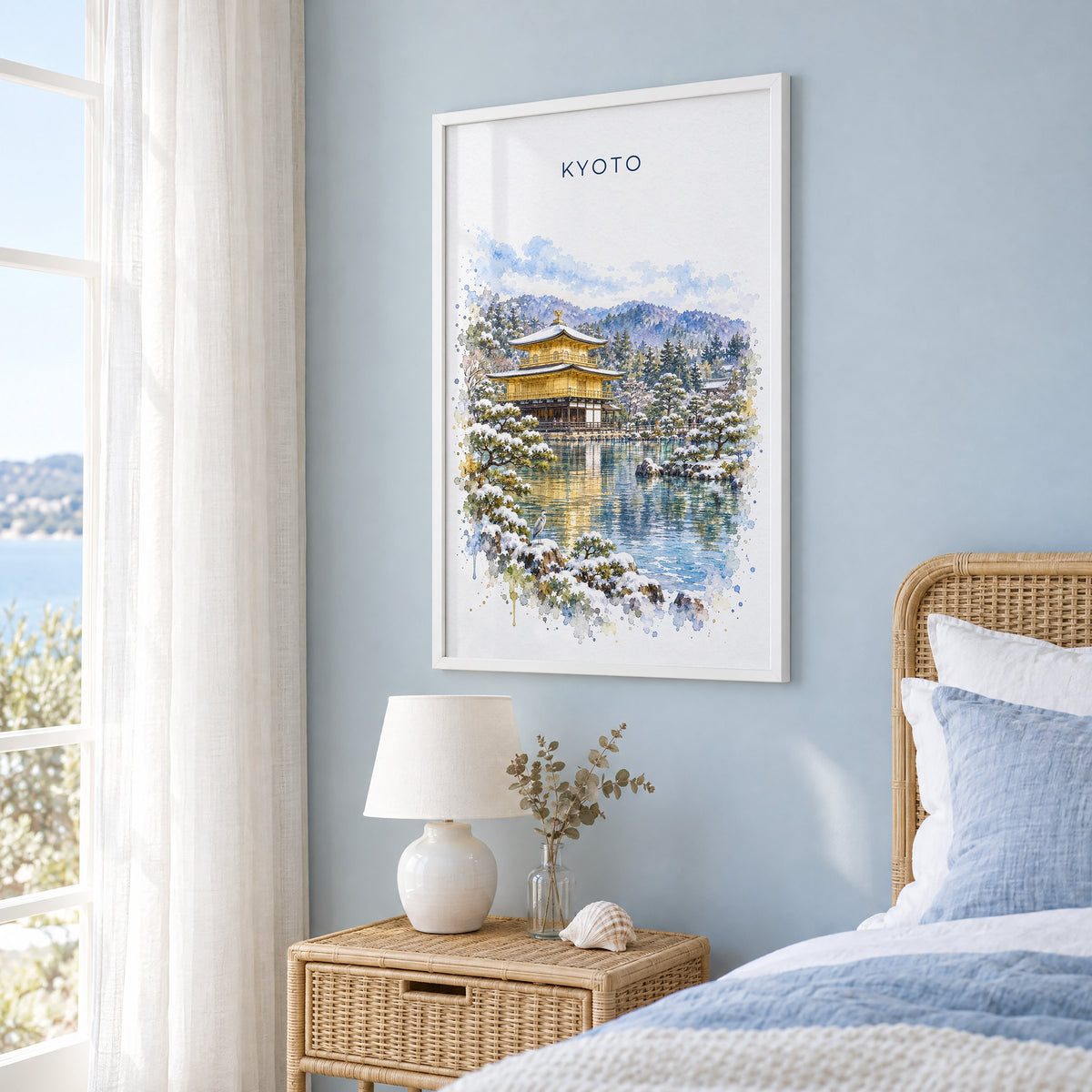 Kinkaku-ji watercolor print in a white frame on a pale blue wall beside a rattan bed in a coastal bedroom