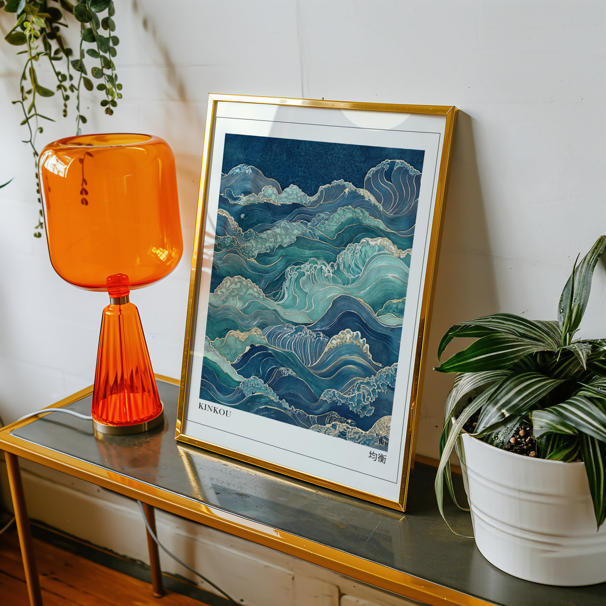 Kinkou teal and gold waves print shown in a gold frame on a console beside an orange glass lamp