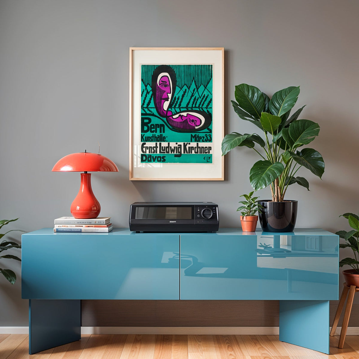 Kirchner poster in an oak frame above a teal sideboard with a red lamp