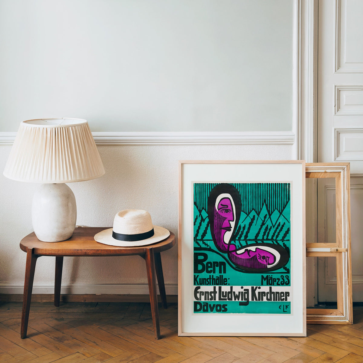 Kirchner typography poster in a light wood frame leaning by a bench and hat