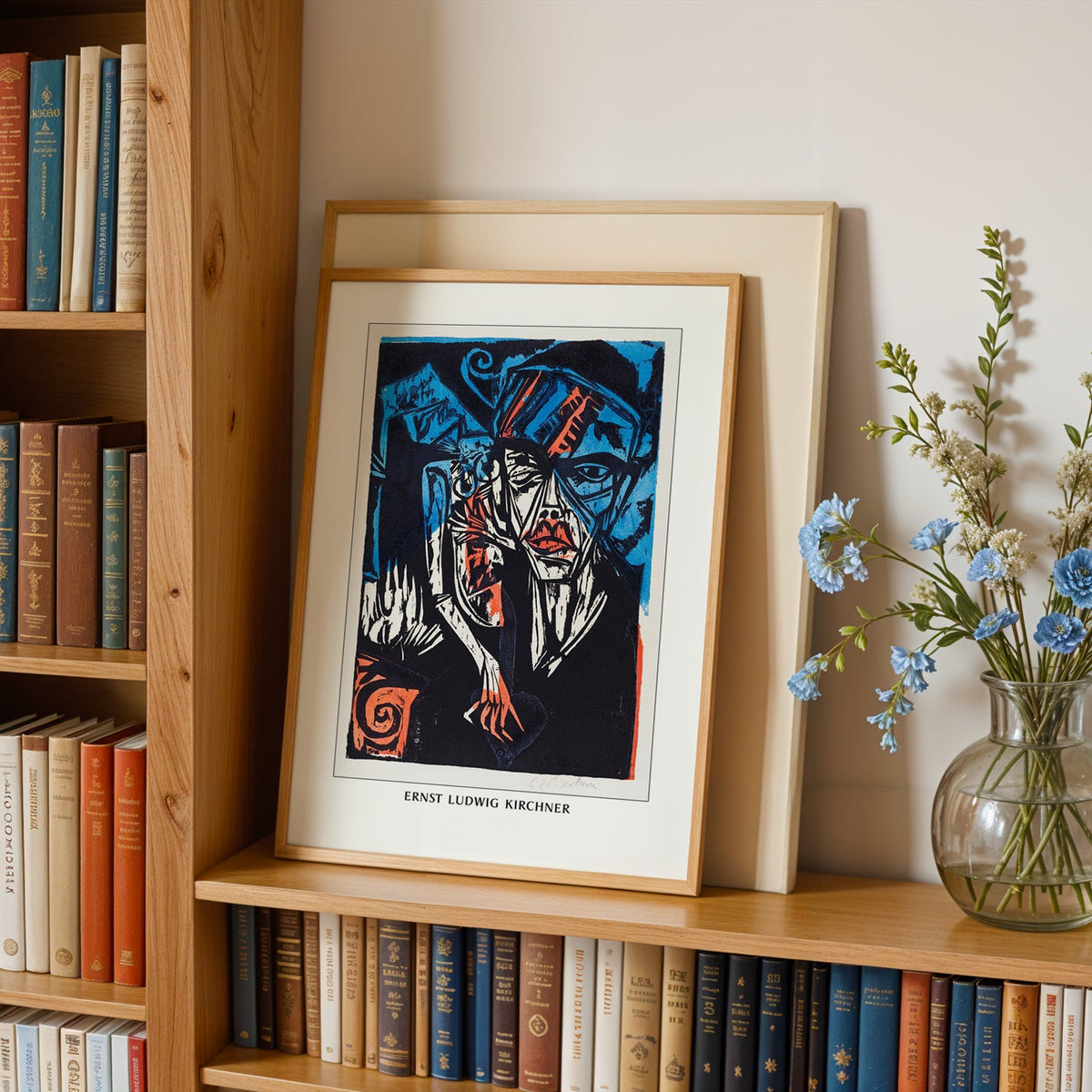 Expressionist print in an oak frame leaning on a bookshelf beside blue flowers