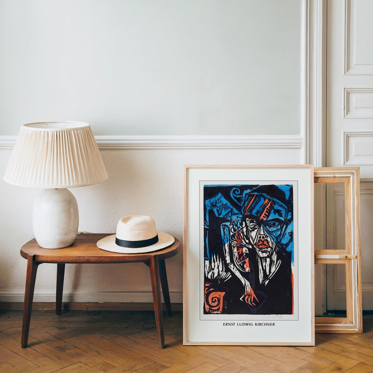 Woodcut poster in a light wood frame leaning by a bench and panama hat