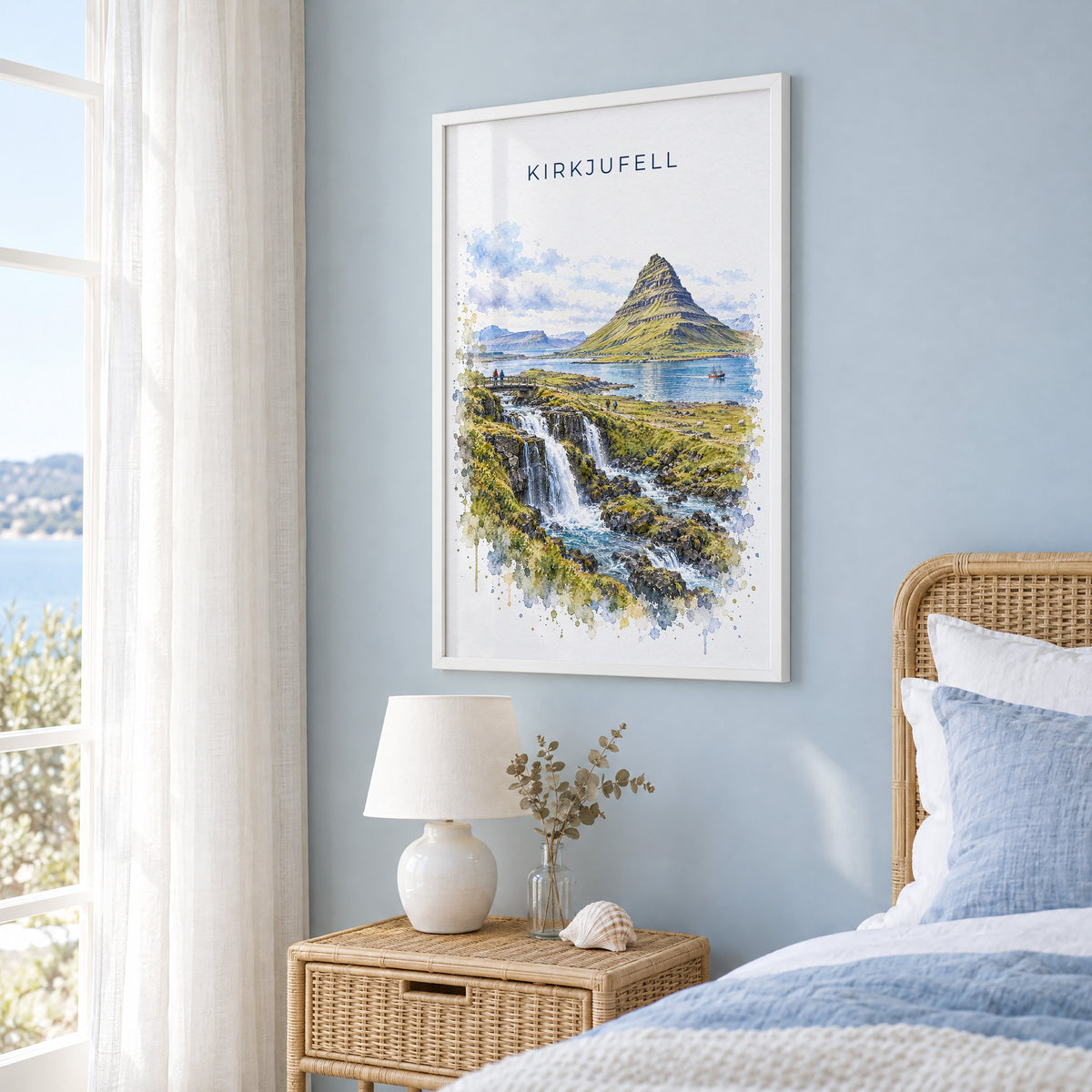 Kirkjufell watercolor print in a white frame on a pale blue wall beside a rattan bed in a coastal bedroom