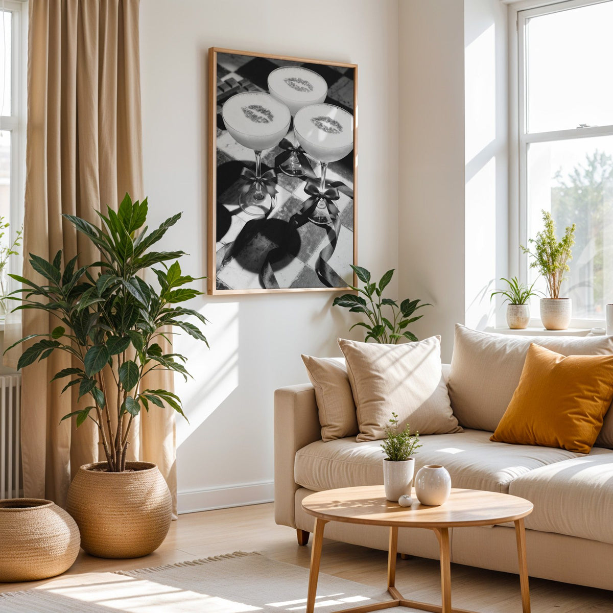 Three coupe cocktails with kiss marks and bows print in an oak frame above a cream sofa beside woven planters