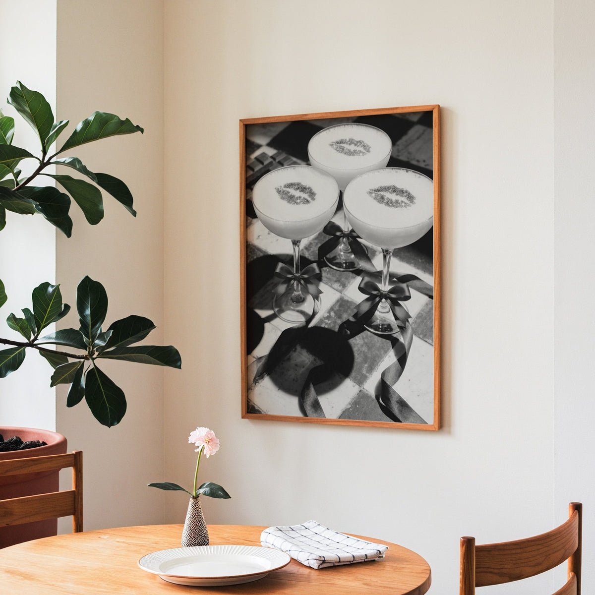 Three coupe cocktails with kiss marks and bows print in a teak frame above a round wooden dining table