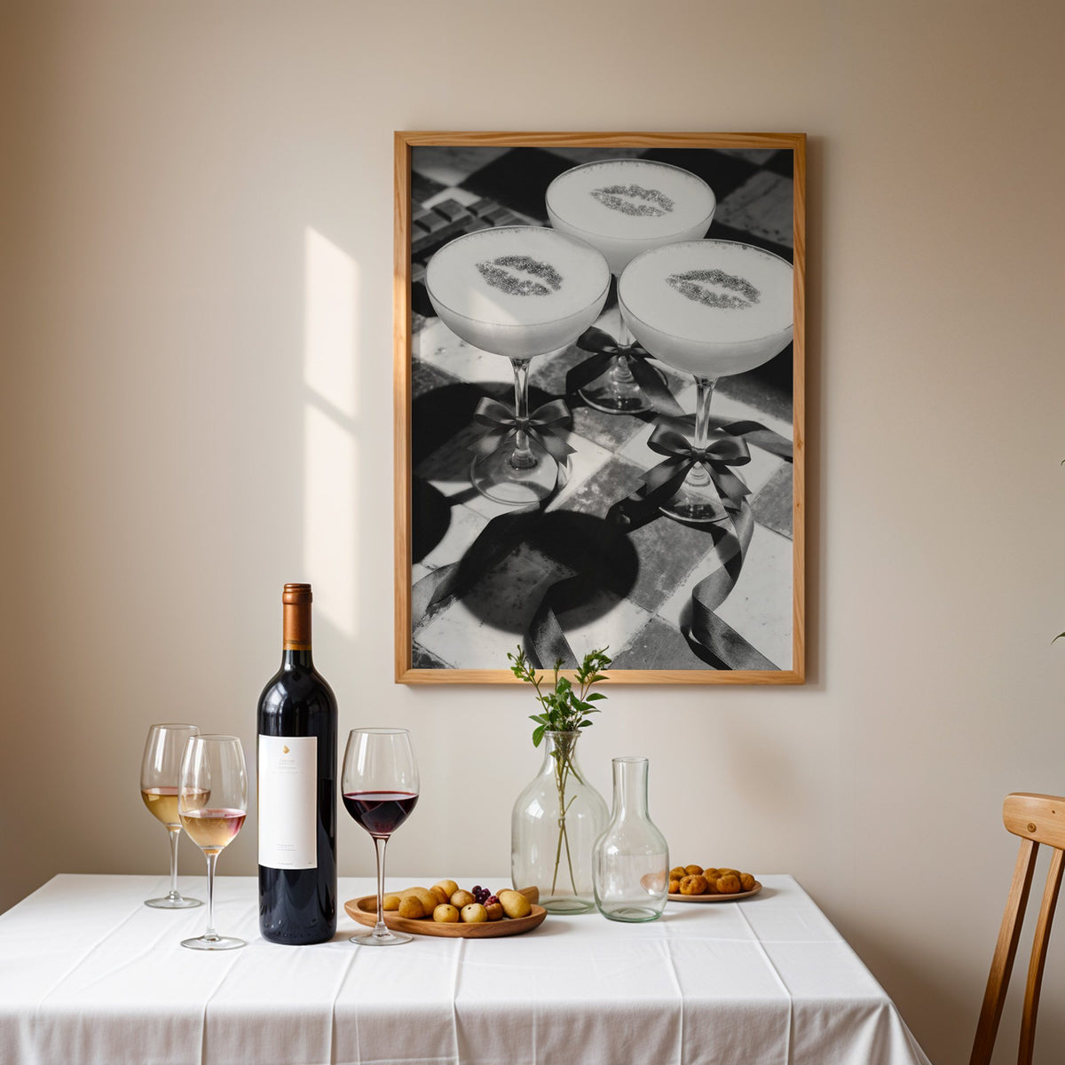 Three coupe cocktails with kiss marks and bows print in an oak frame above a table set with red wine and glasses