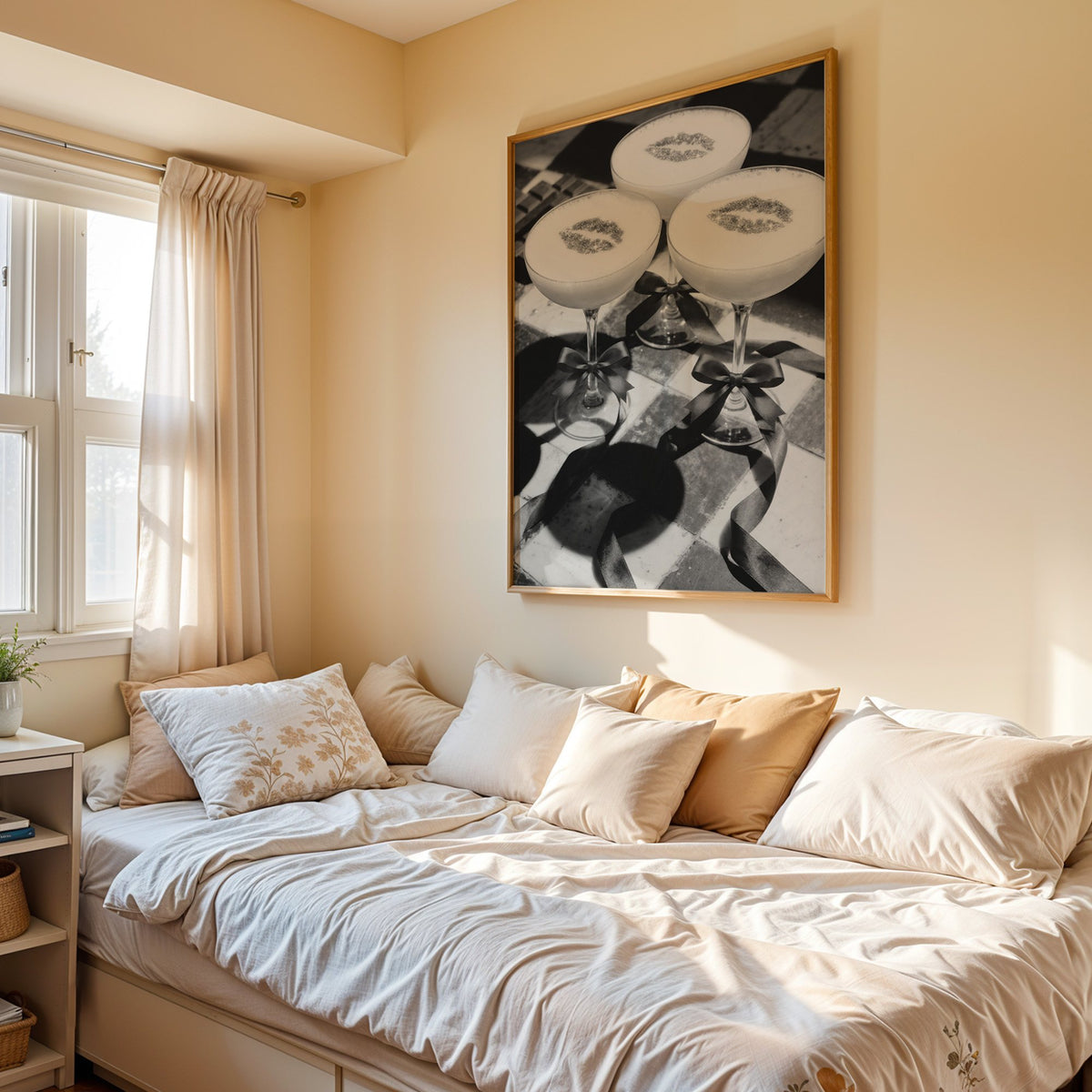 Three coupe cocktails with kiss marks and bows print in an oak frame above a cream daybed in a sunny bedroom