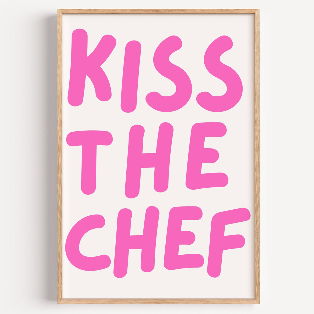 Kiss the Chef typography print in a light oak frame on a plain white wall