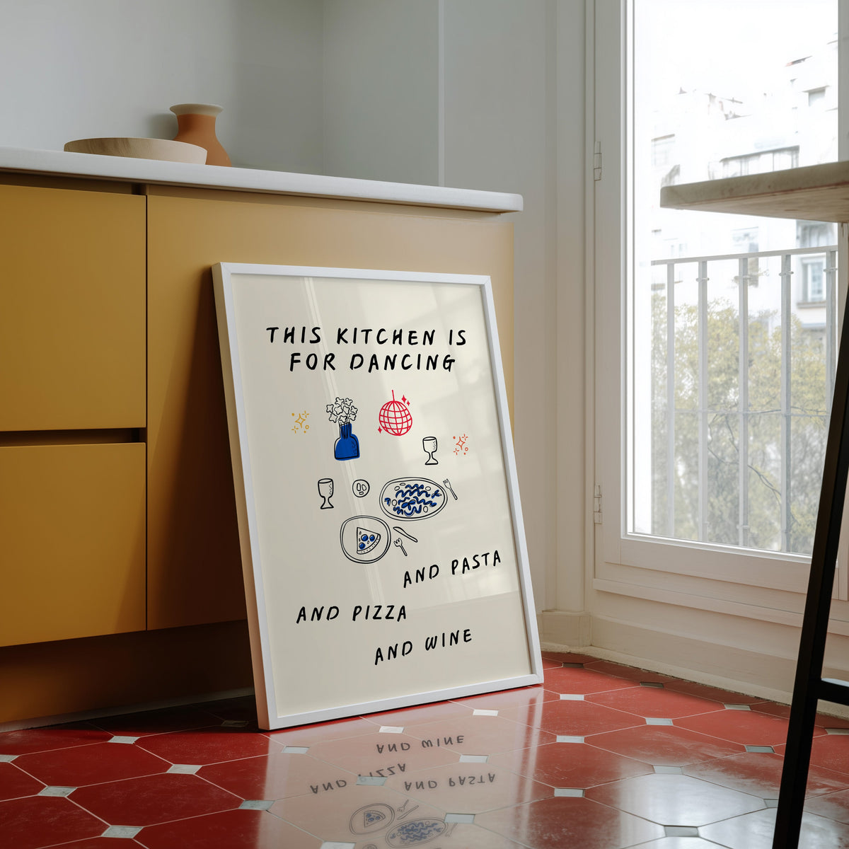 Kitchen Is For Dancing print in a white frame against yellow cabinets on a red tiled floor