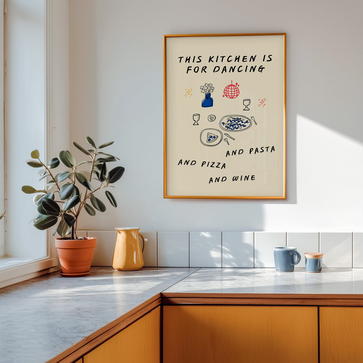 Kitchen Is For Dancing print shown in a gold frame above a marble counter with a yellow ceramic jug
