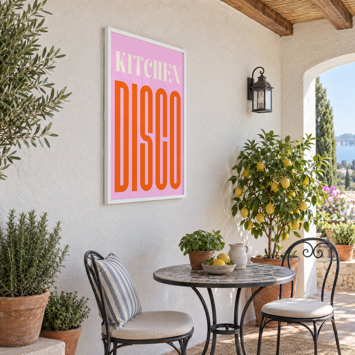 Kitchen Disco pink and orange type print in a white frame on a sunny patio wall beside a potted lemon tree