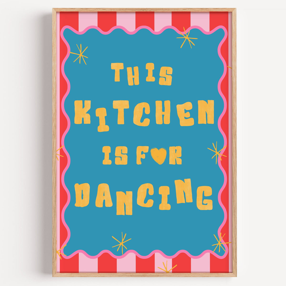 This Kitchen Is For Dancing blue print in a light oak frame on a plain white wall