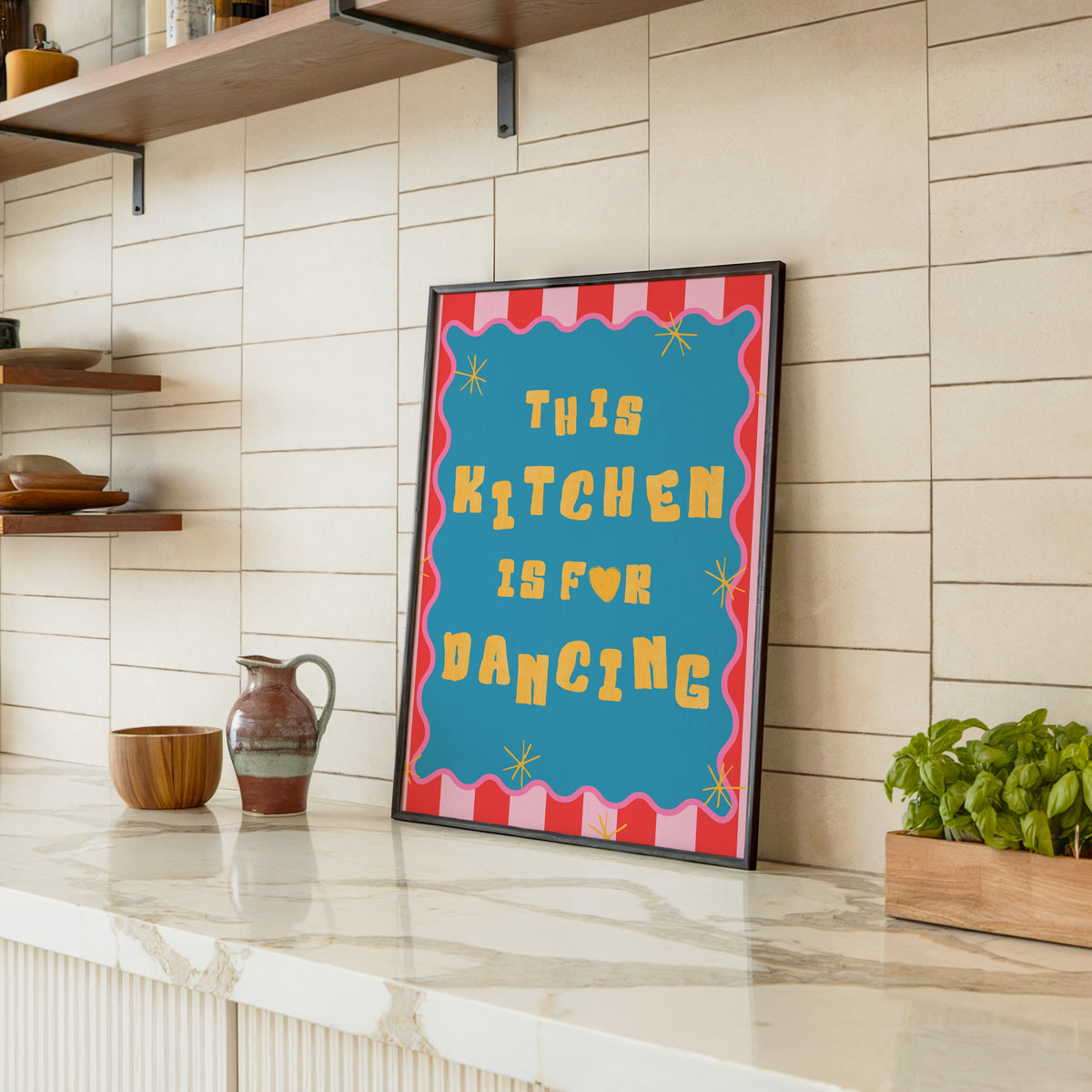 This Kitchen Is For Dancing print in a black frame leaning on a marble counter in a tiled kitchen