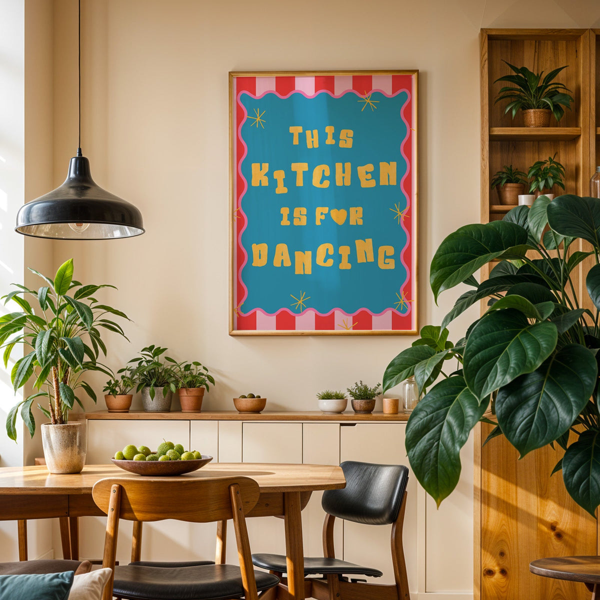 This Kitchen Is For Dancing print in an oak frame in a dining room above a plant-lined sideboard
