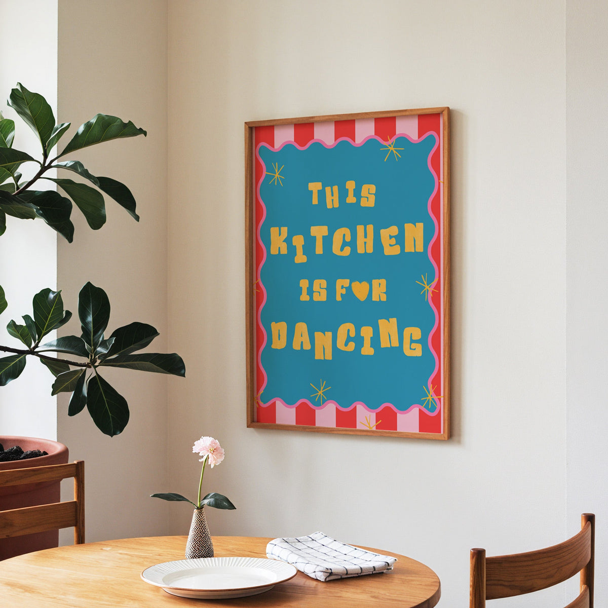 This Kitchen Is For Dancing print in a walnut frame above a round table beside a fiddle-leaf fig