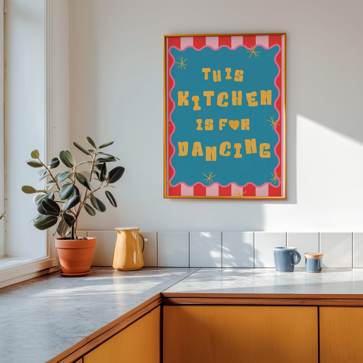 This Kitchen Is For Dancing print shown in a gold frame above a marble counter in a tan kitchen