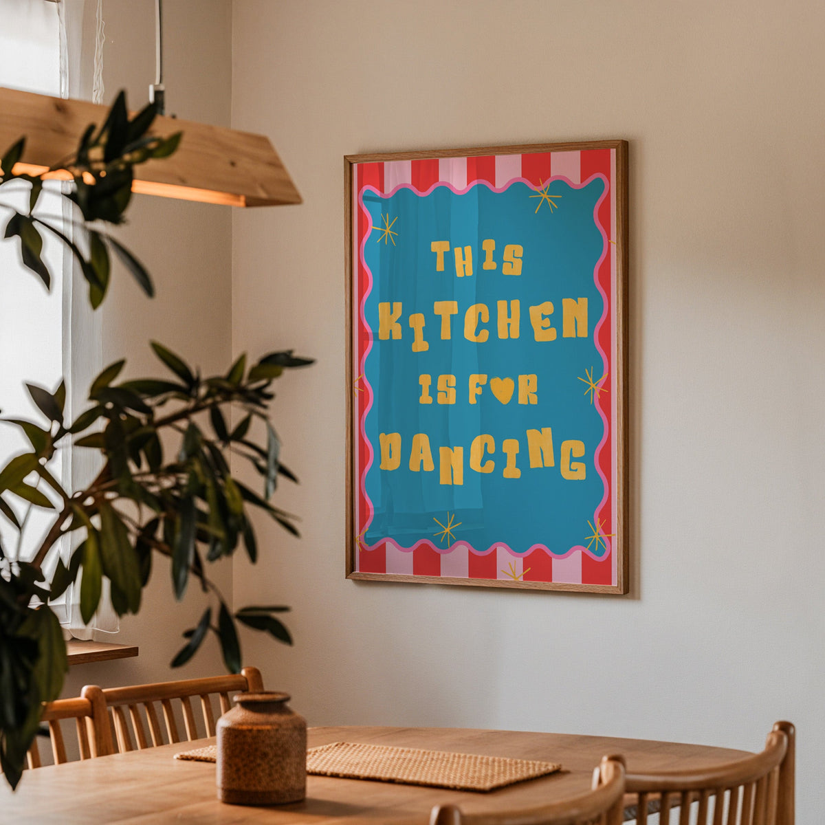 This Kitchen Is For Dancing print in a walnut frame above a dining table with olive branches