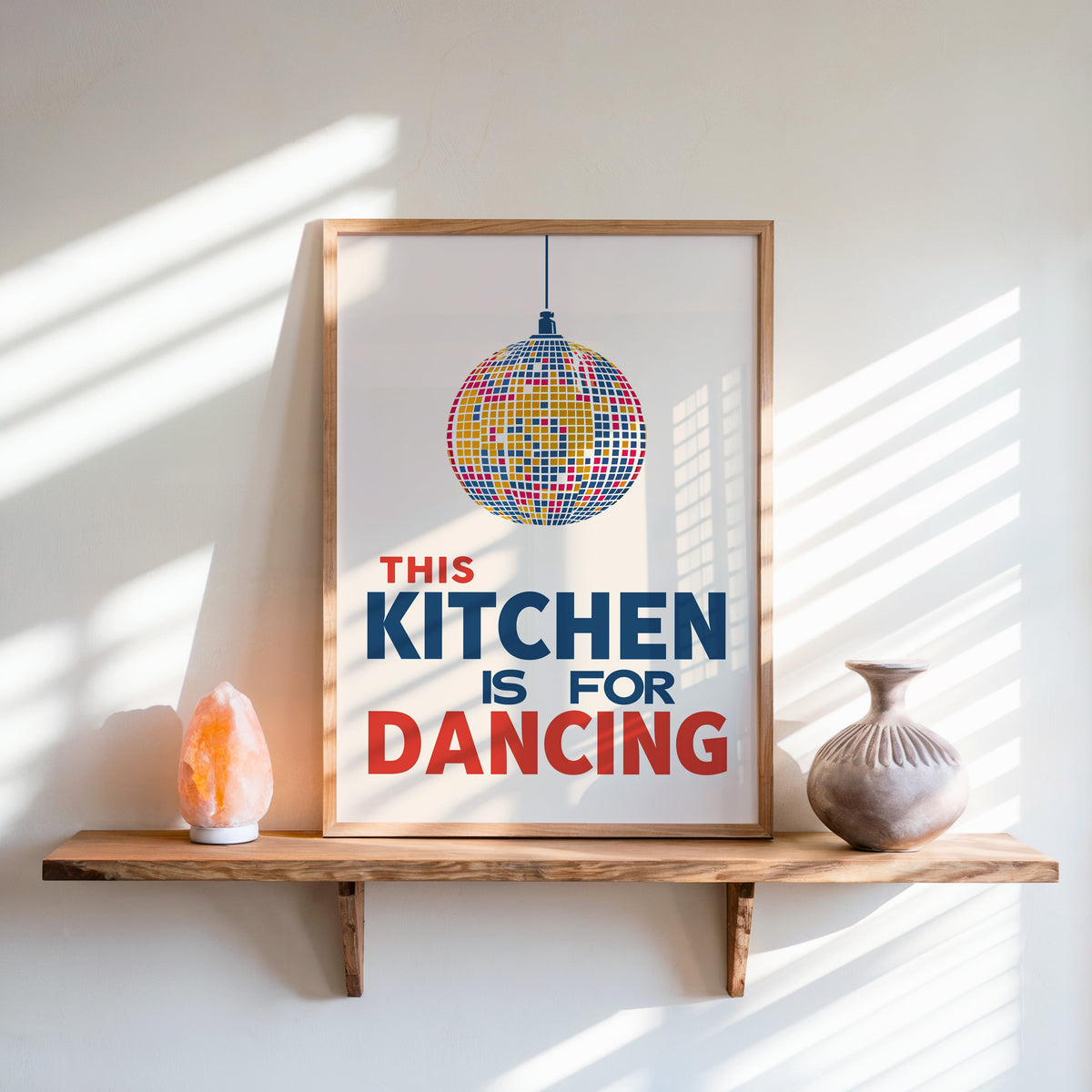Kitchen Is For Dancing blue disco print in an oak frame on a live-edge shelf beside a salt lamp