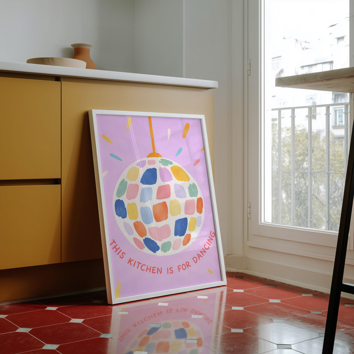 Pastel disco ball print in a white frame against yellow cabinets on red tiles