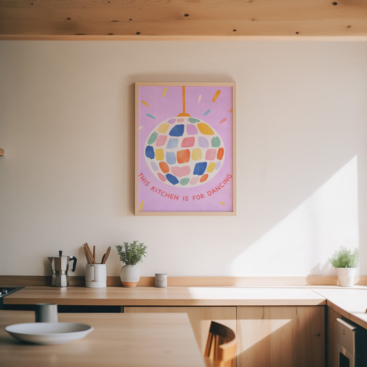Pastel disco ball print in an oak frame above a wood counter with a moka pot