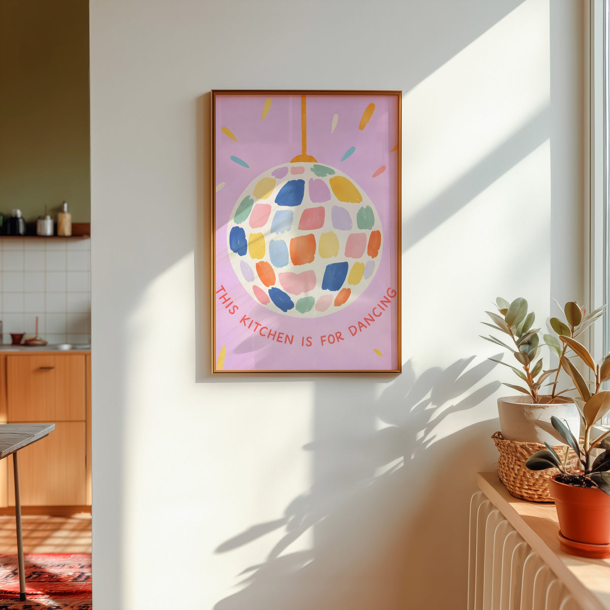 Pastel disco ball print in a gold frame in sunlight with plants and a kitchen beyond