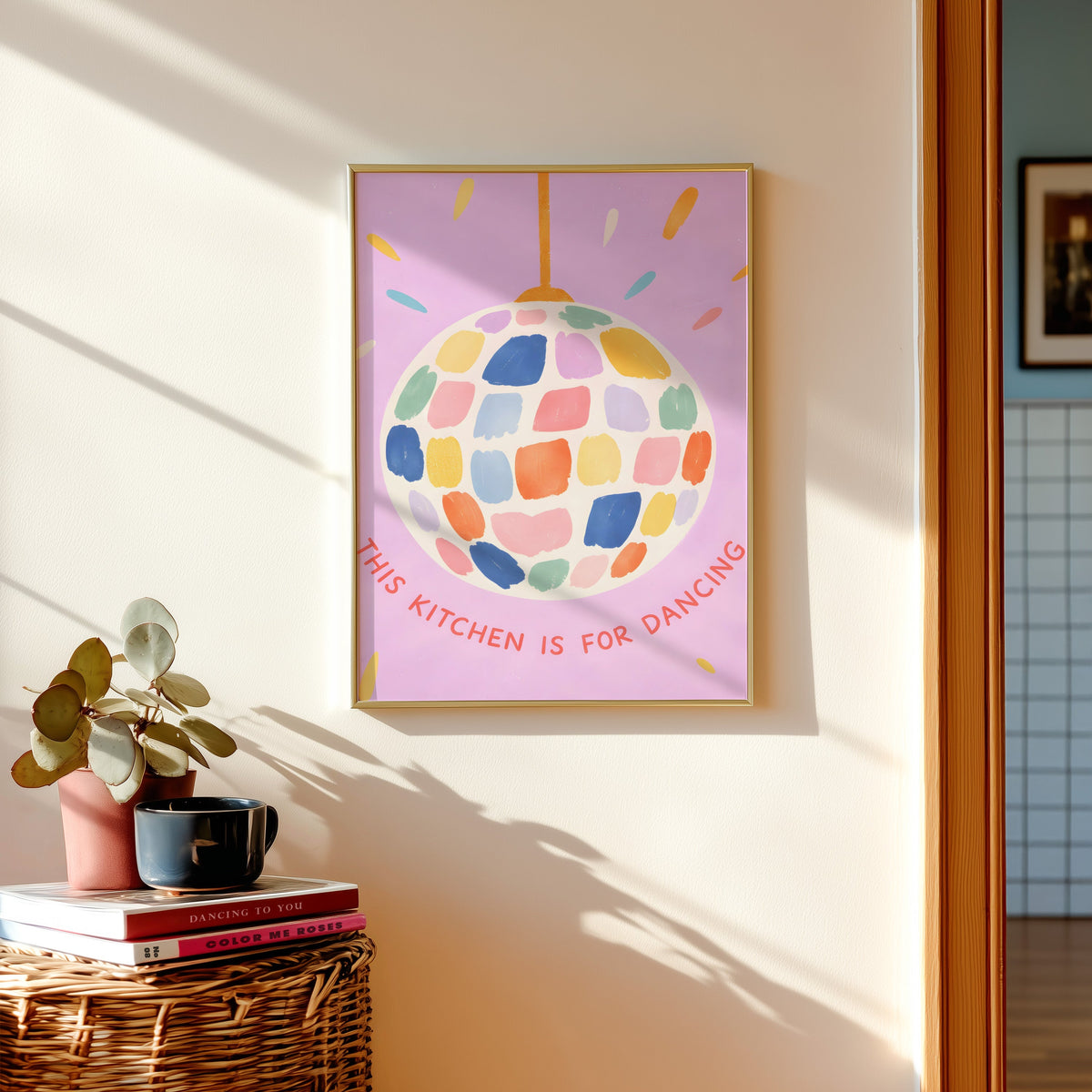 Pastel disco ball print in a gold frame above a basket of books and a pilea plant