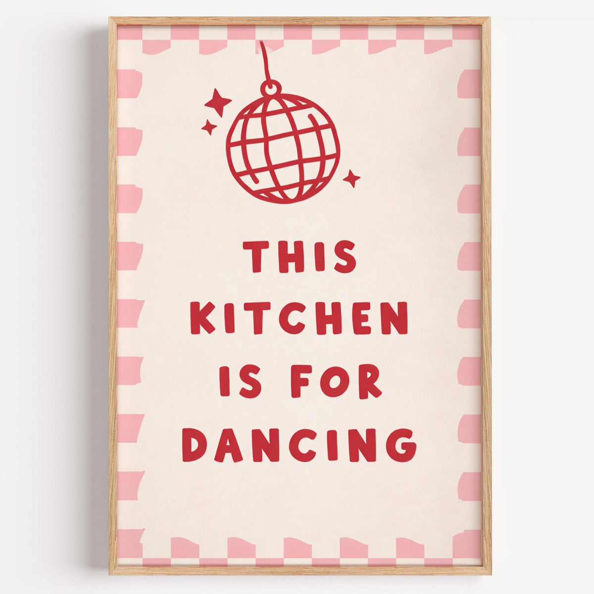 Kitchen Is For Dancing pink check disco print in a light oak frame on a plain white wall