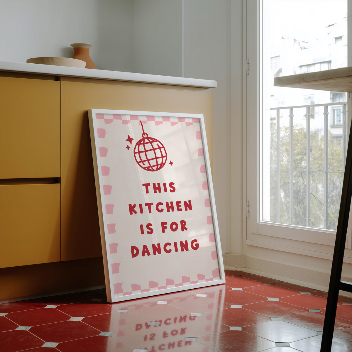 Kitchen Is For Dancing pink check print in a white frame against yellow cabinets on a red tiled floor